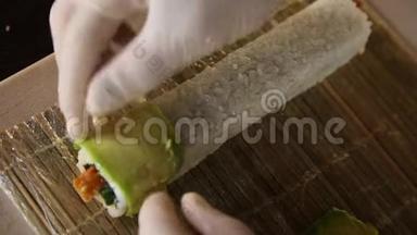 寿司大师的手在竹席上用鳄梨片装饰寿司卷。 寿司制作工艺。 把寿司卷滚起来